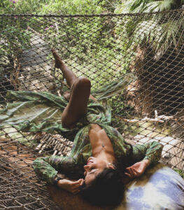 A scene at Azulik Hotel in Mexico, capturing a woman relaxing on a mesh hammock surrounded by lush tropical greenery, exuding tranquility.