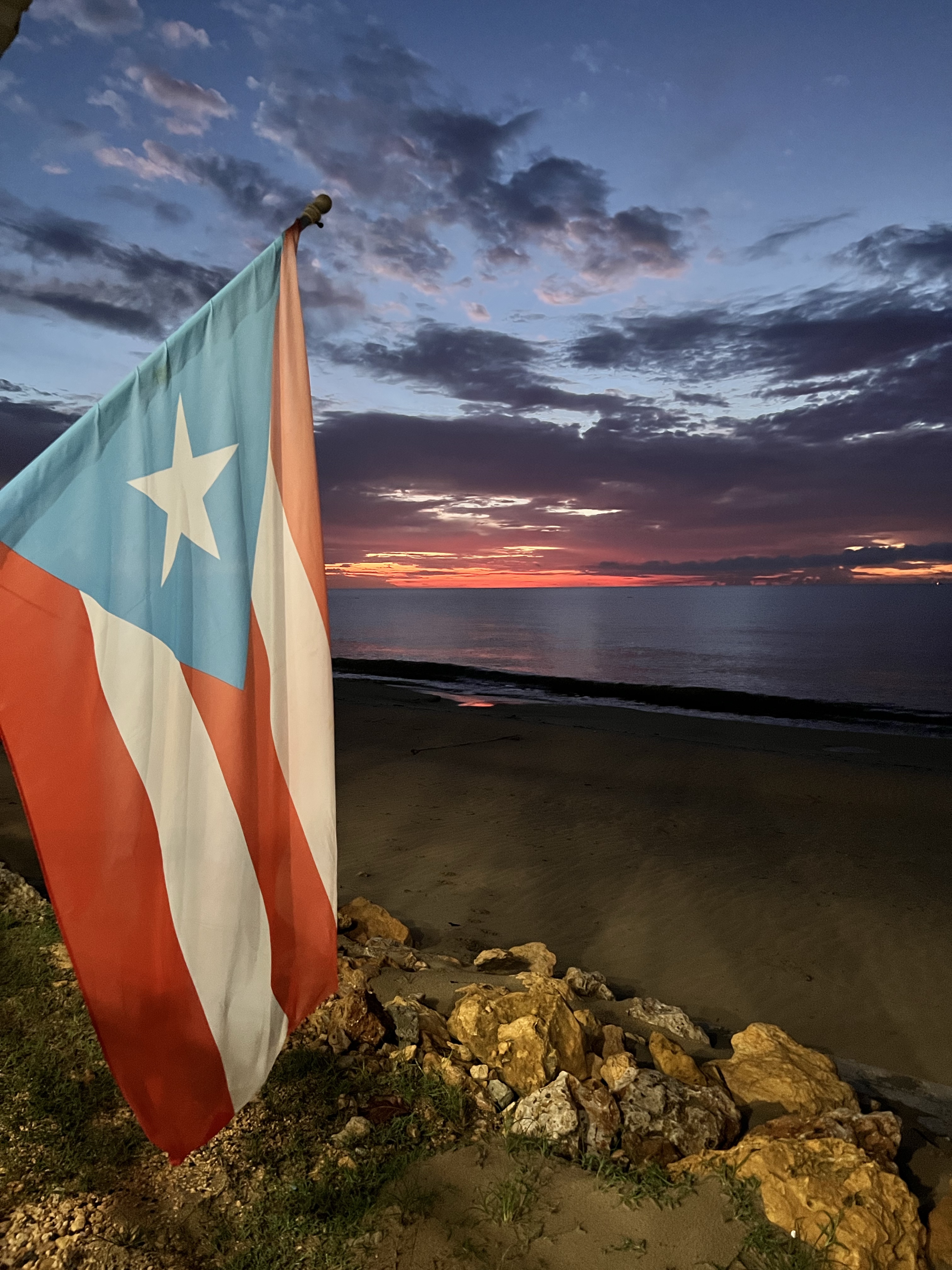 Puerto Rican flag waving against a sunset over the ocean