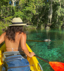 A woman kayaking in clear waters with a sea turtle nearby.